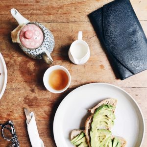 tea, teapot, and avocado toast on a light brown wooden table